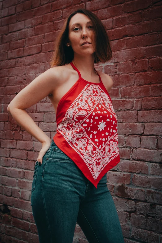 a woman with a bandanna over her neck stands against a brick wall