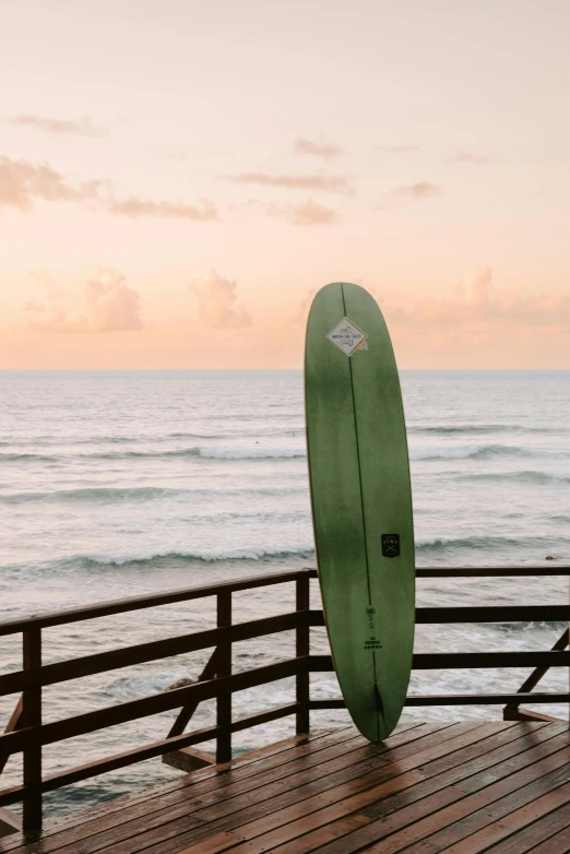 a green surf board stands on a wooden deck