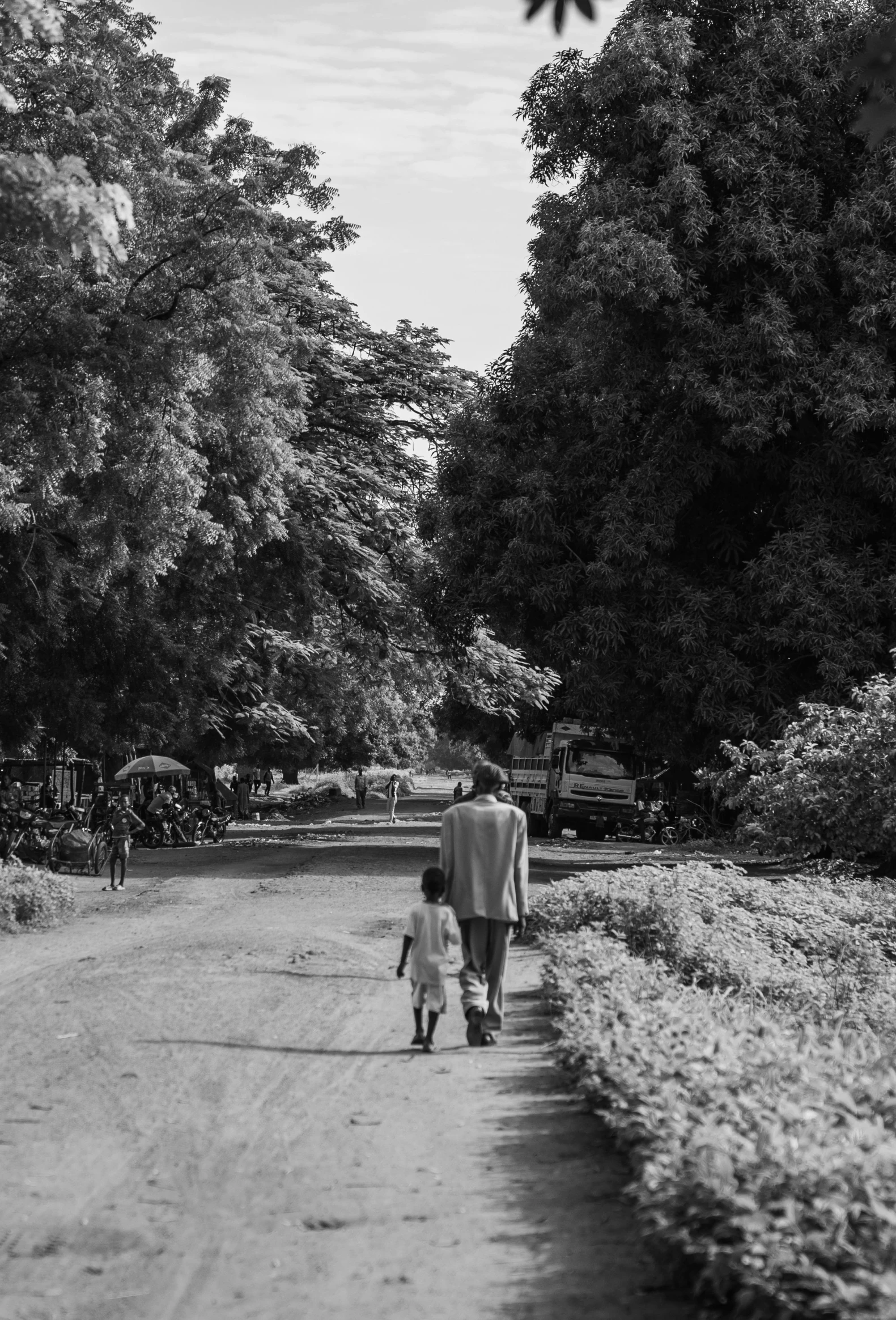 a man and woman walking down the path next to trees