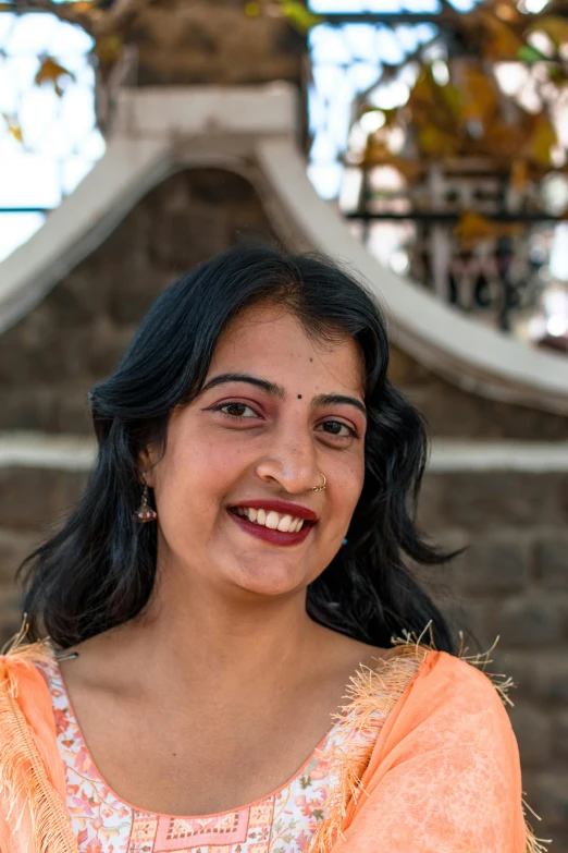 woman smiling outside near old building and decorative tree