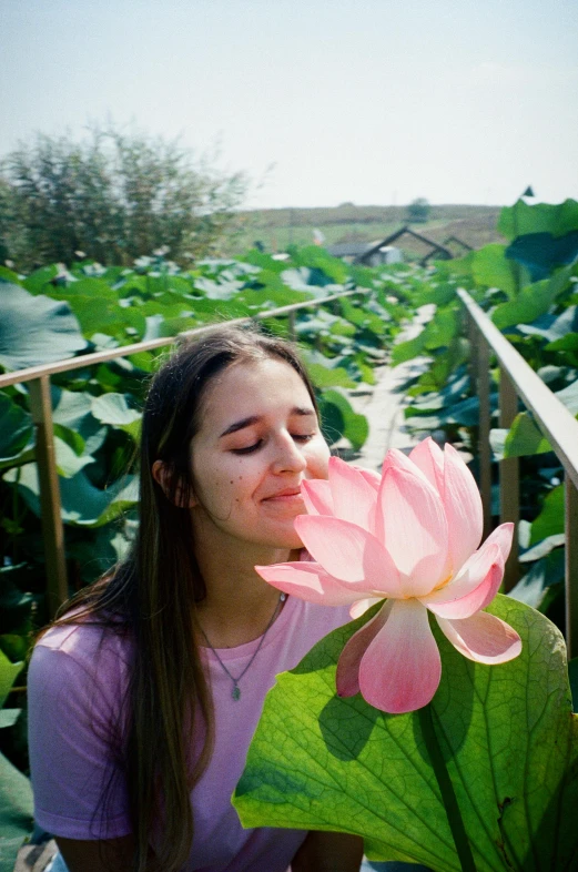 a girl is sitting outside with a pink flower in front of her