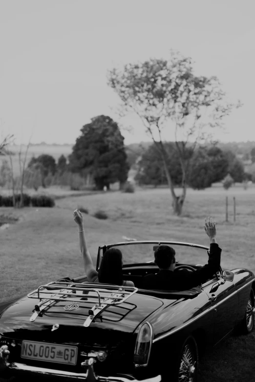 two women sit in a sports car with their arms outstretched