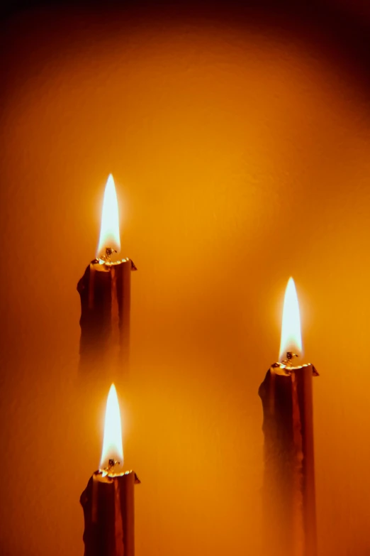 three lit candles in an orange tinted room