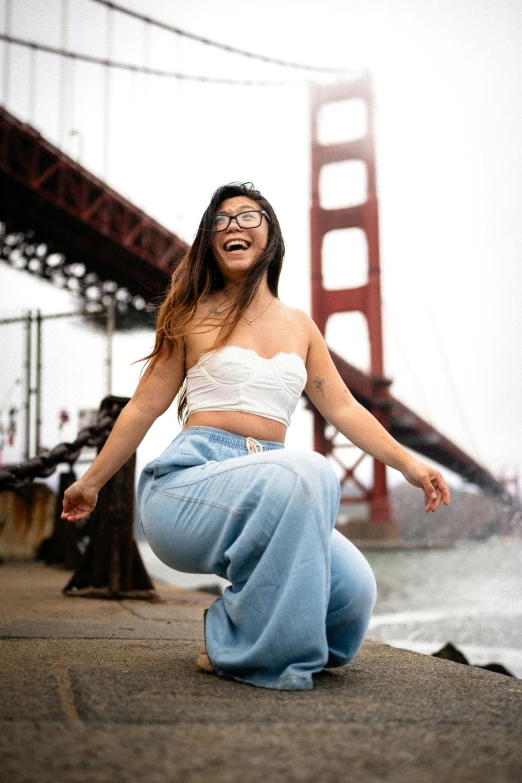 woman in jeans dancing on the pier with bridge in background