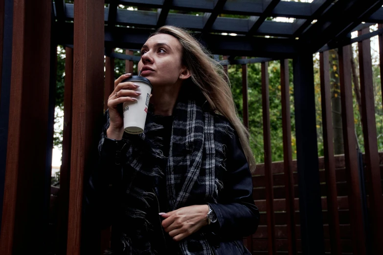 a woman drinking from a coffee mug in front of a wood structure