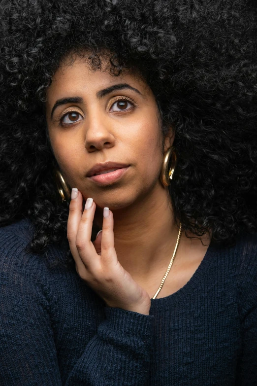 a woman with an afro has her chin up to her right side, looking up, on black background