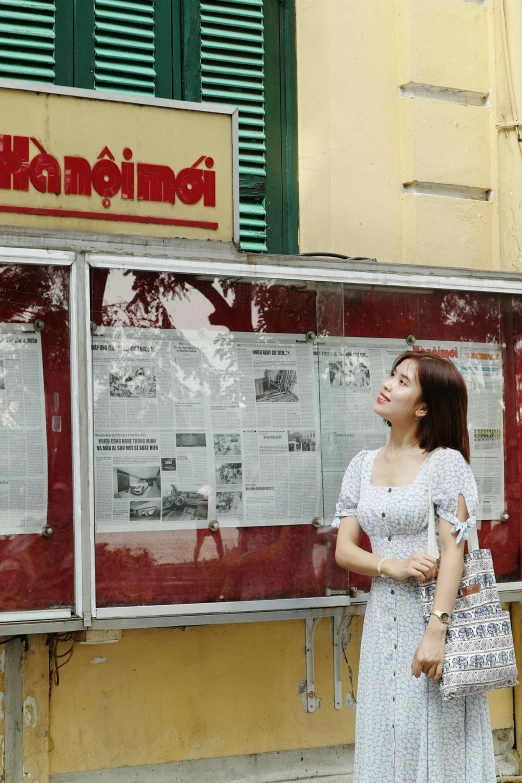 the woman in white is standing near a newspaper stand