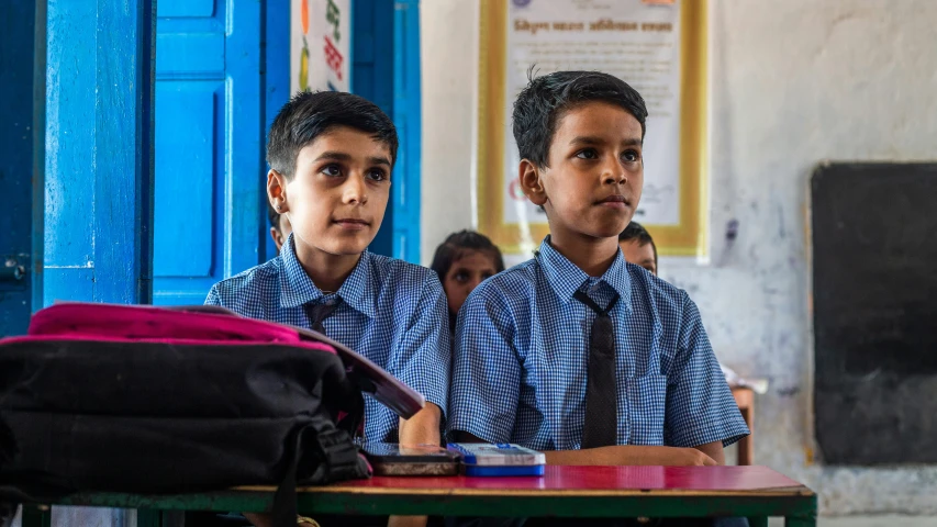 two boys sit on the school desk in their uniforms