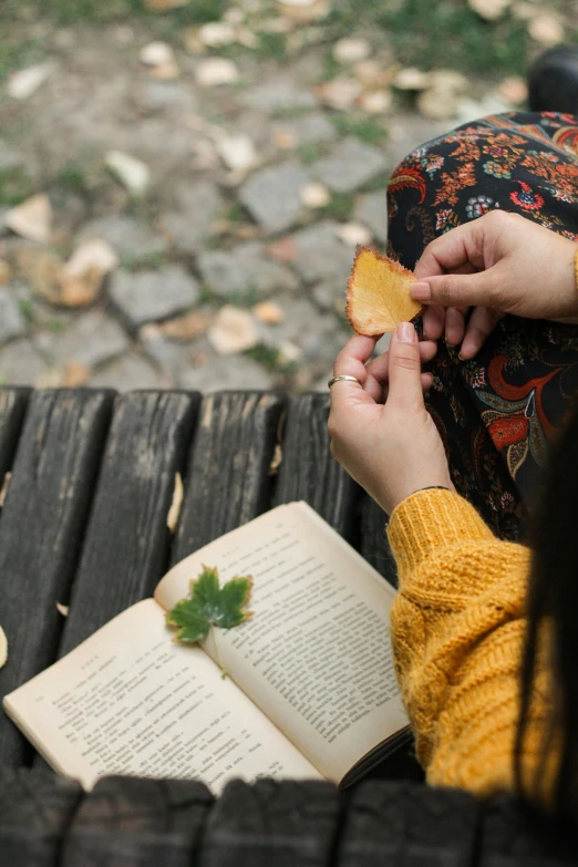 the girl is reading her book and holding a leaf