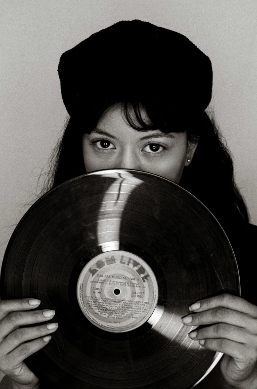 a woman holding up an old record with her face peeking through the cover