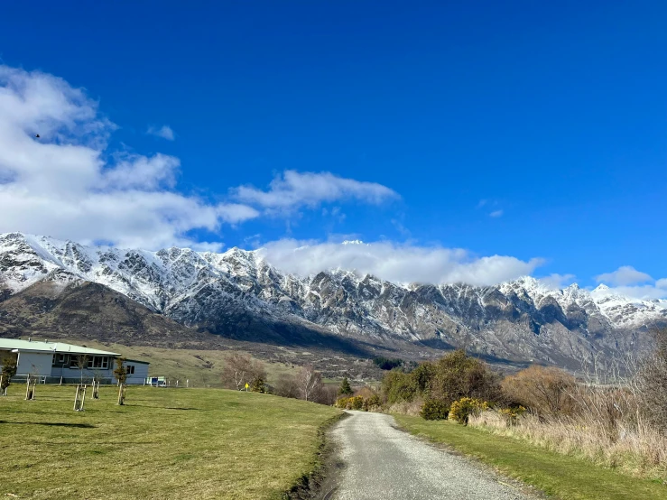 a dirt path leading to mountains with green fields and trees