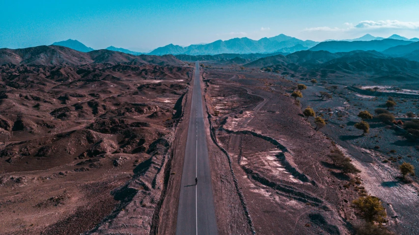 an empty road winding through a desert with mountains in the background