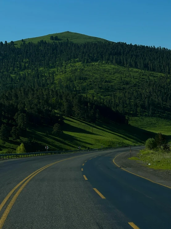 the side of a curved road running past a green hillside