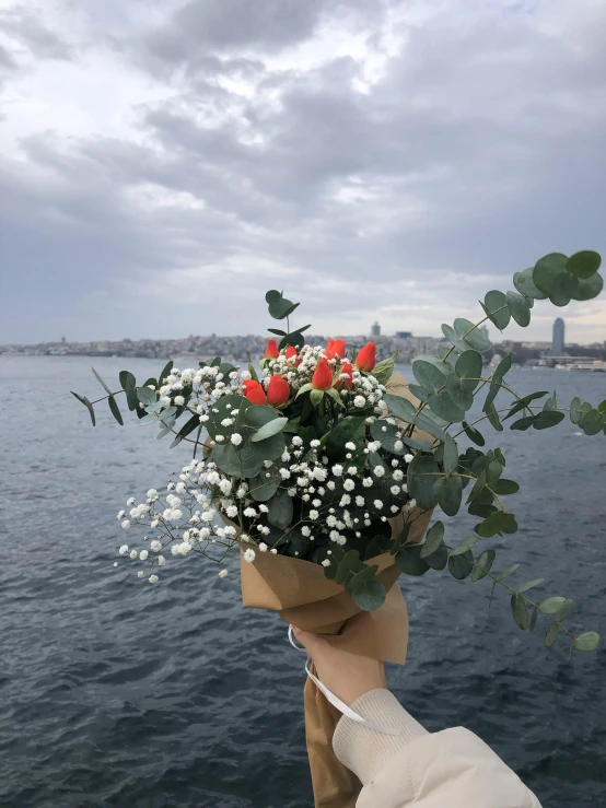 a hand holding onto a bouquet of white and red flowers