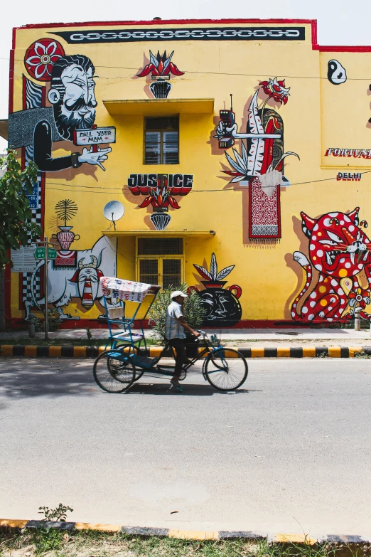 person riding bike near yellow building covered in art