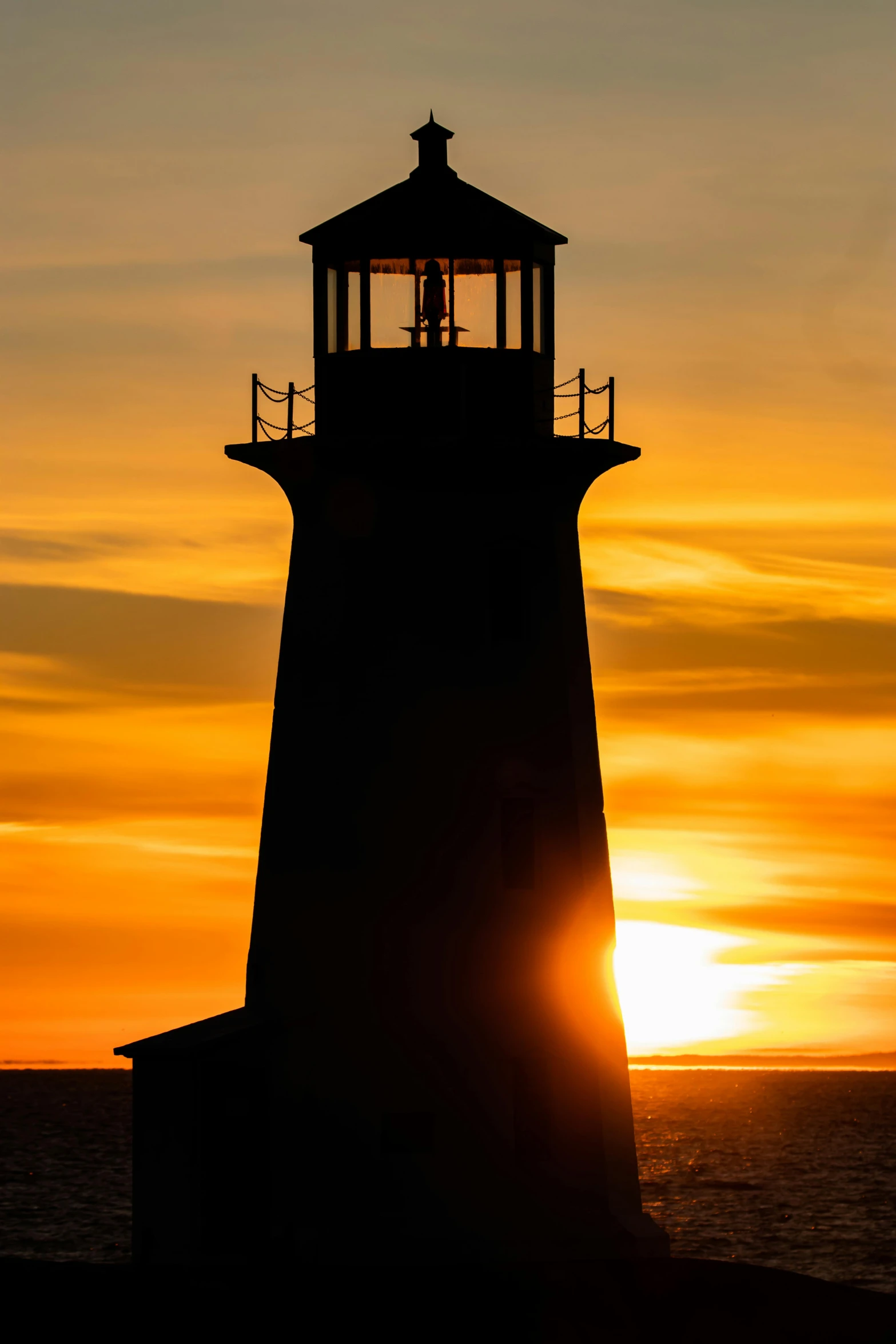 a large light house standing next to the ocean during the sunset