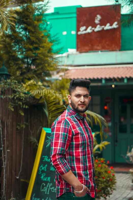 a man is standing on a sidewalk wearing a checked shirt and green pants