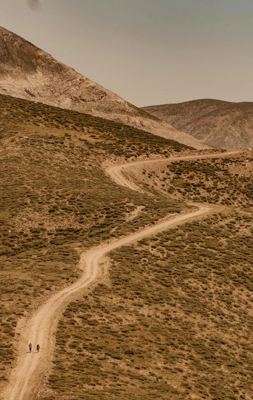 two people walking up a hill on a trail