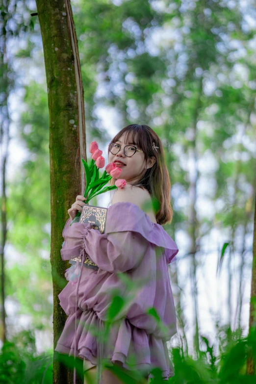 a woman holding flowers in a forest with trees in the background