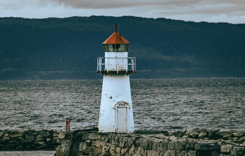 a lighthouse sitting on the shoreline with mountains in the background