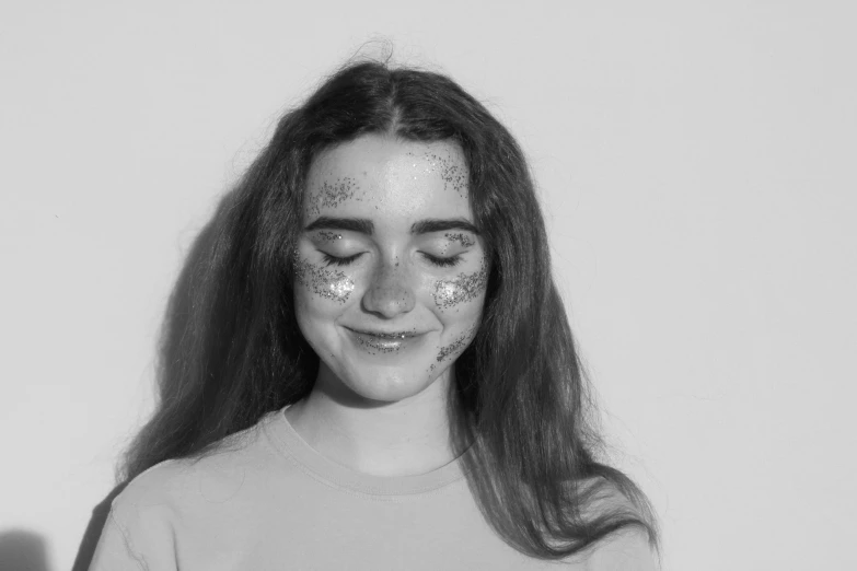 a woman with sequins on her face standing against a white wall