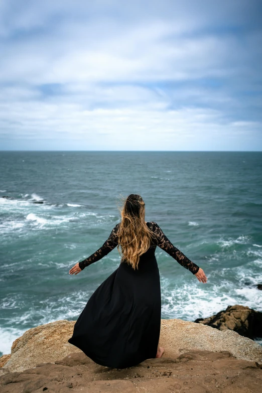 a woman sitting on a rock looking out at the ocean