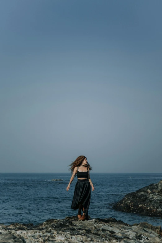 the woman standing on rocks is alone by the ocean