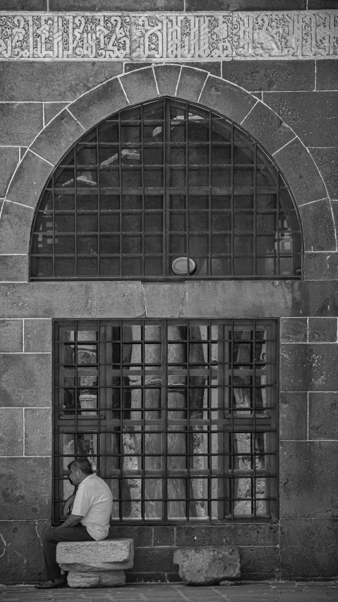 a black and white po of a man sitting outside a  cell door