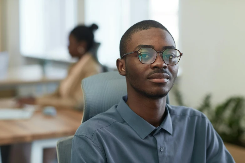 man in blue shirt with glasses sitting at his desk