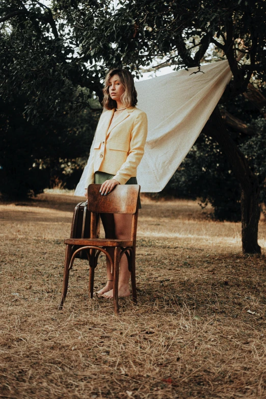 a woman in yellow jacket sitting on wooden chair in field