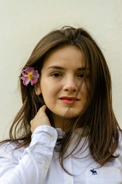 a woman with long hair, wearing a white shirt and a flower in her hair