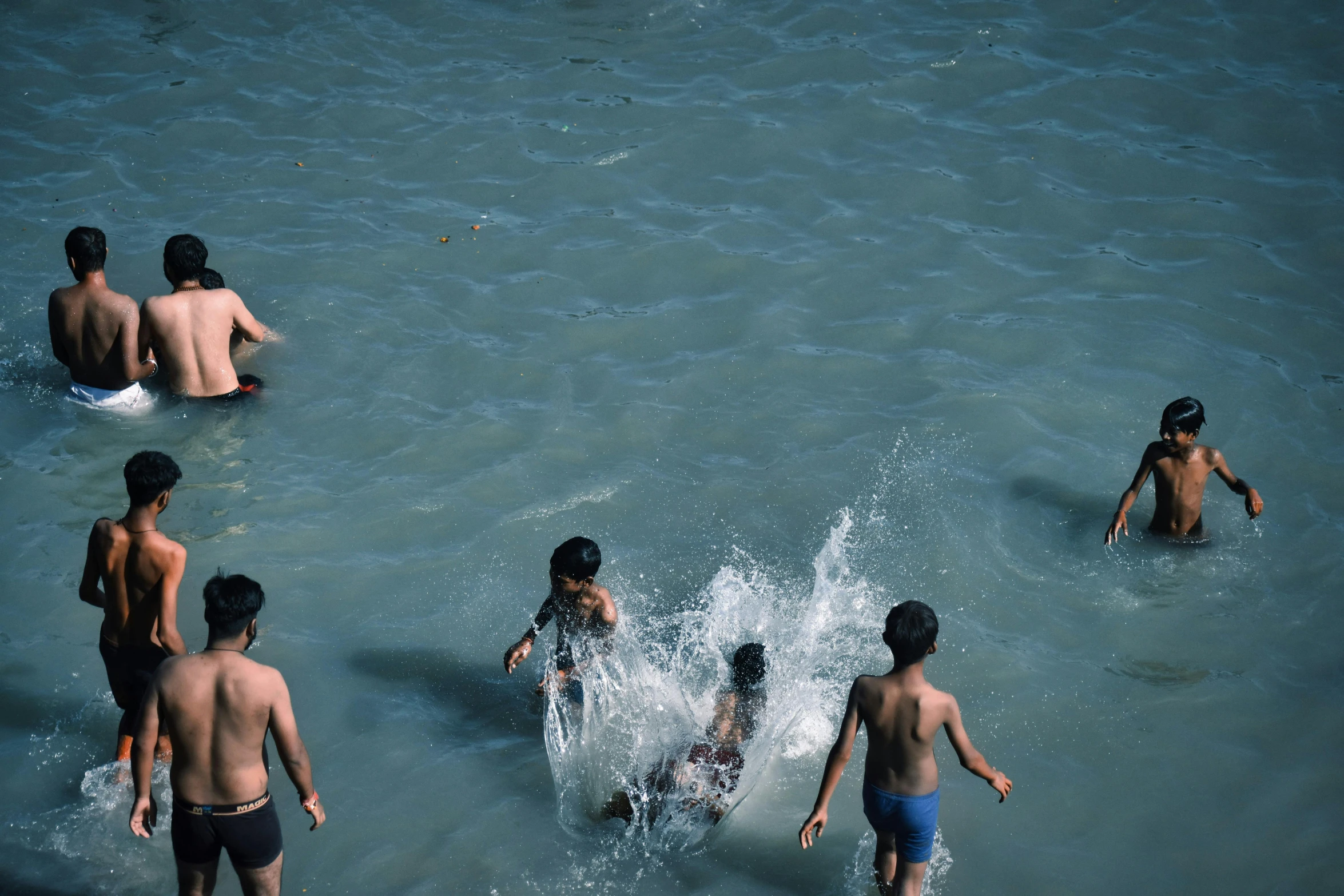 several children playing in the water while one boy watches