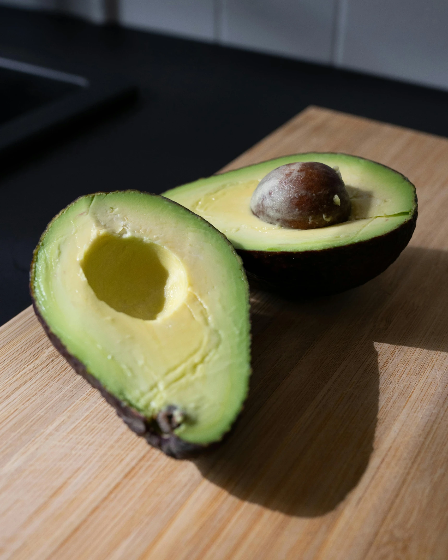 an avocado sliced in half and half opened on a  board