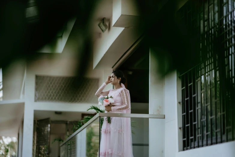 woman in pink standing outside of a building while talking on a cell phone