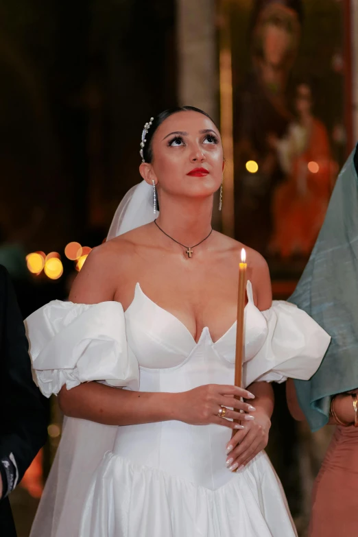 a woman wearing a wedding dress carrying a lit candle in her hand