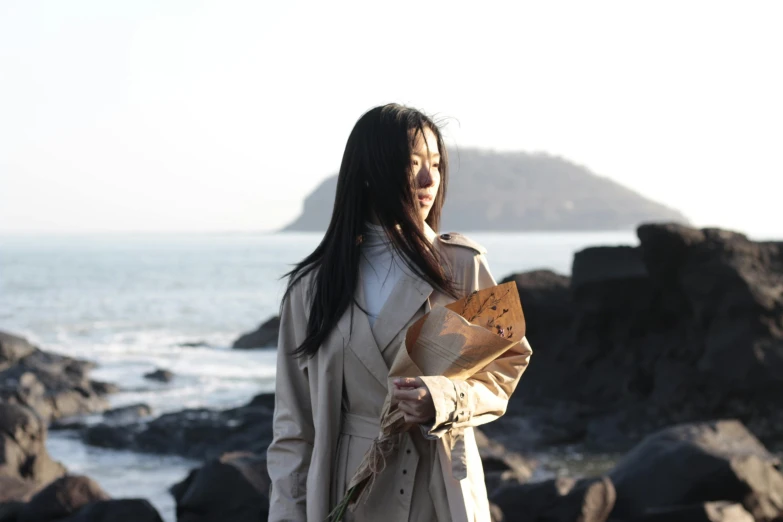 woman standing in front of the ocean holding flowers