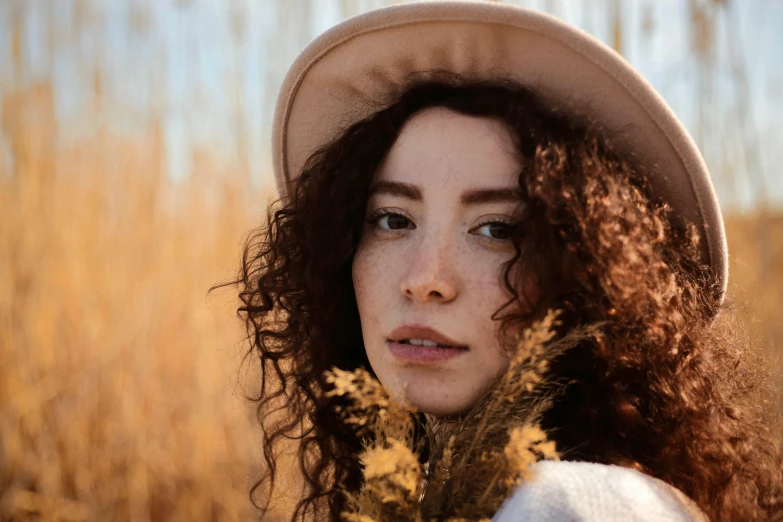 a woman wearing a hat is standing near a field