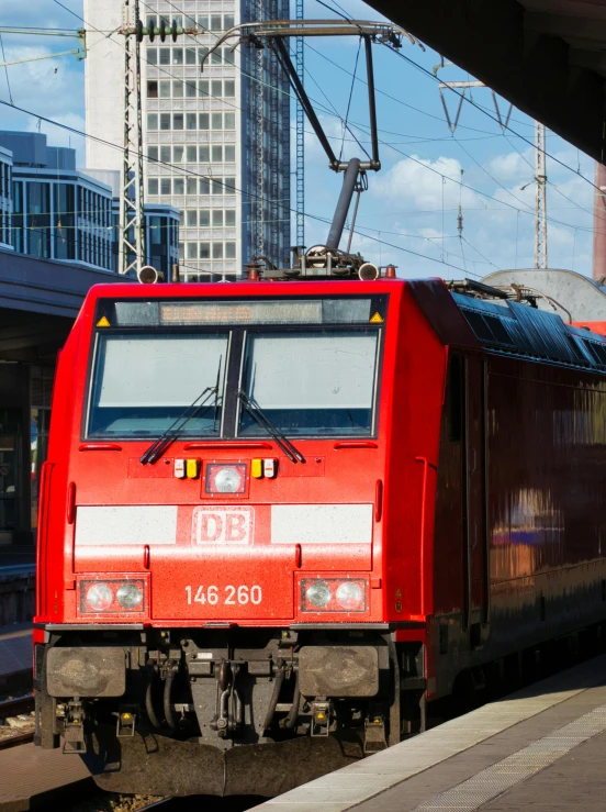 a red passenger train with a big building behind it