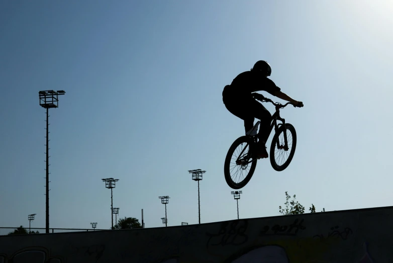 a silhouette of a man jumping his bicycle into the air