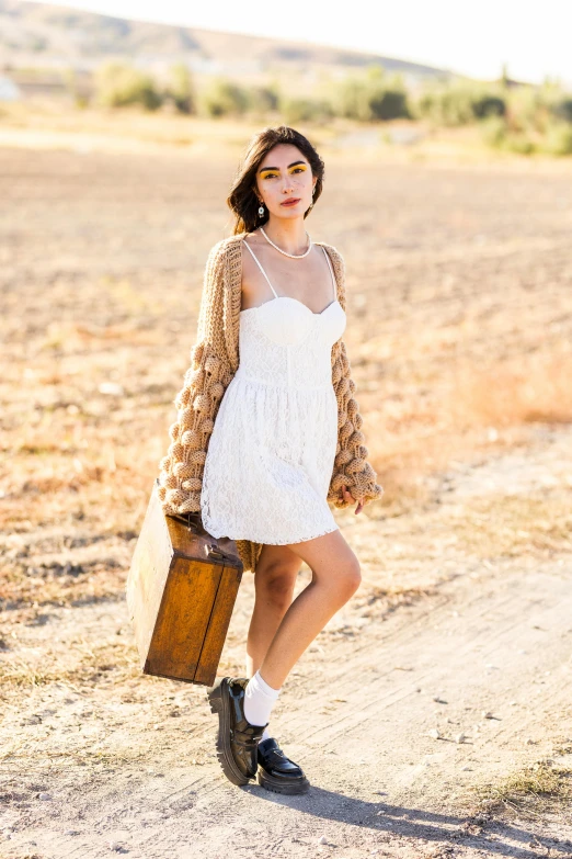 a woman with an open jacket, white dress and brown briefcase standing in dirt field