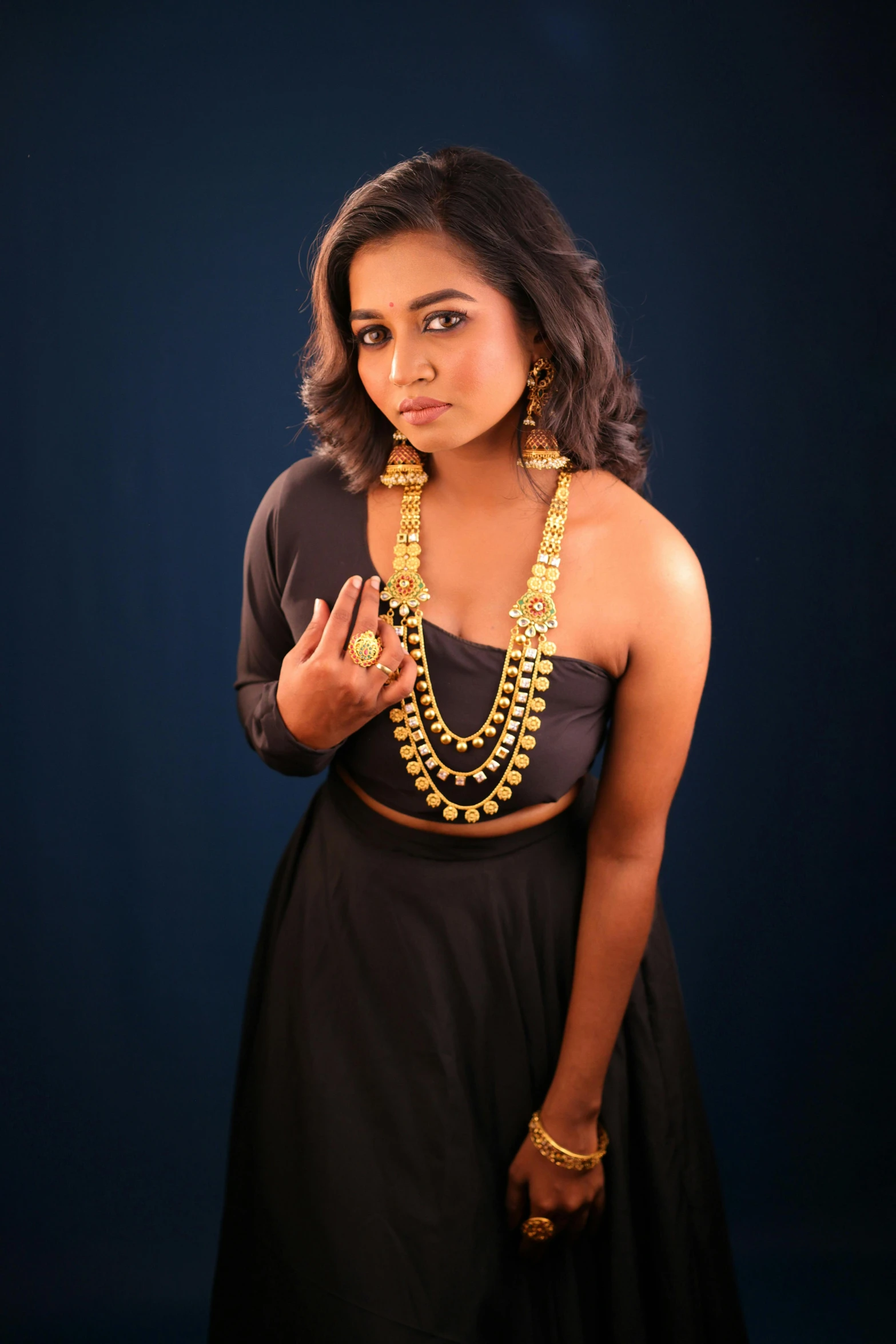 a young woman wearing gold necklaces with a hand holding up a peace sign
