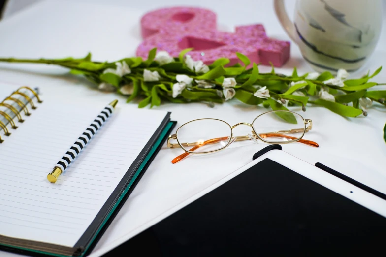 a notebook, flower, books and pen lay on a desk