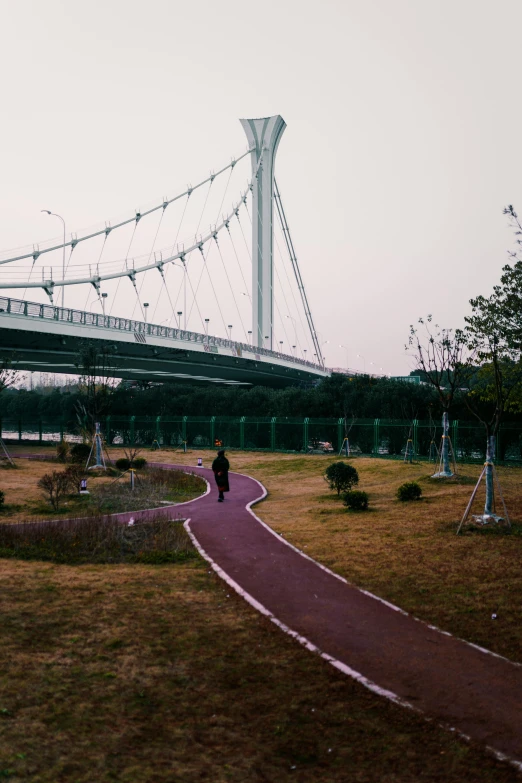 a person walks across a path next to a large bridge