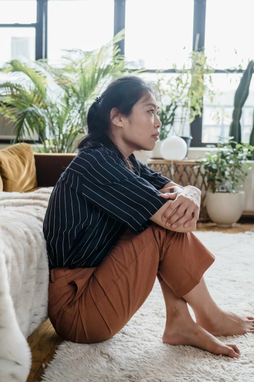 a woman is sitting on the floor and looking out of her window