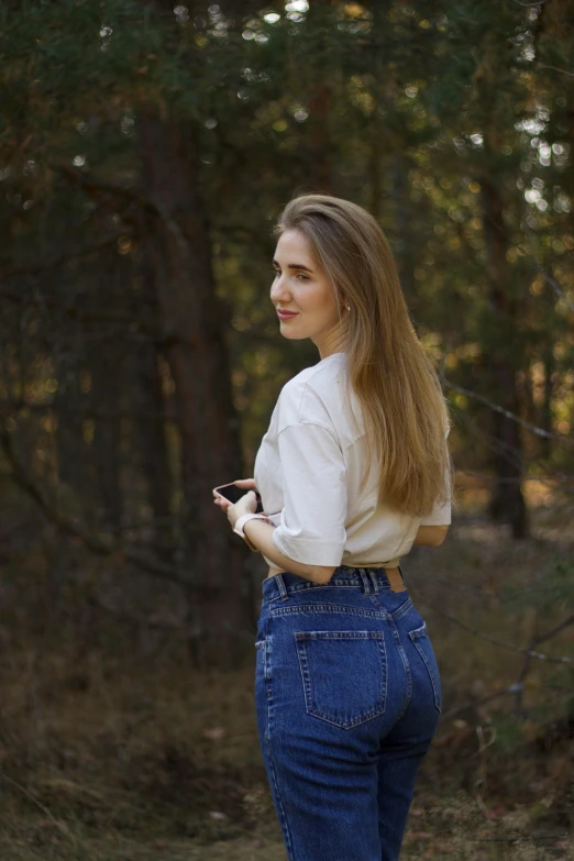 a young woman standing next to a forest holding a cell phone