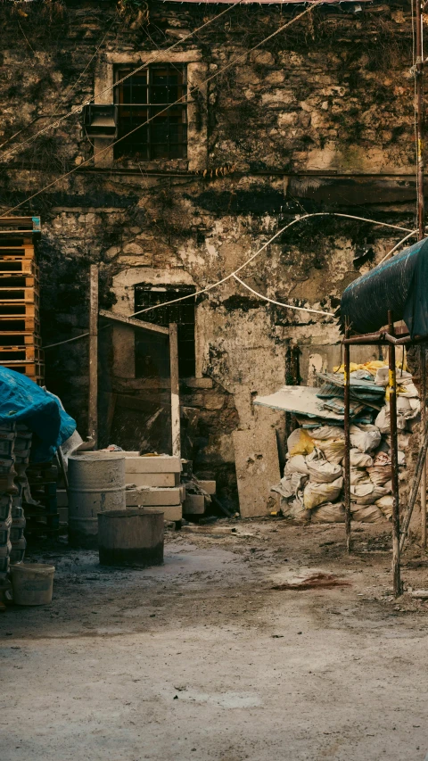 a brick building with broken windows, a blue tarp, a bed and some potted plants