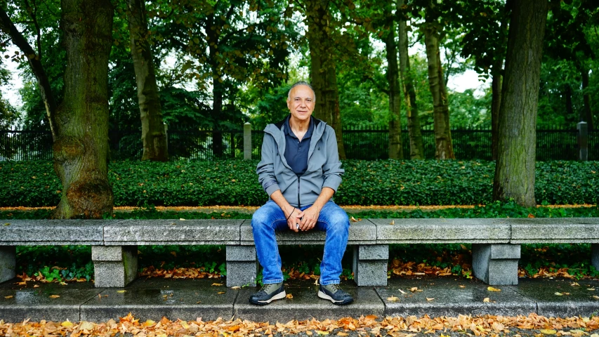 the man sits on a bench with trees and leaves