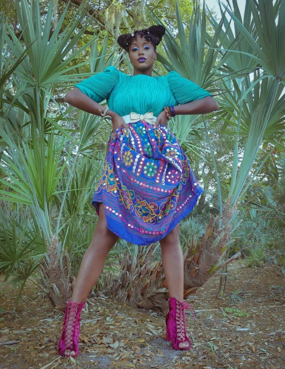 a black woman in bright clothes poses with her arms folded