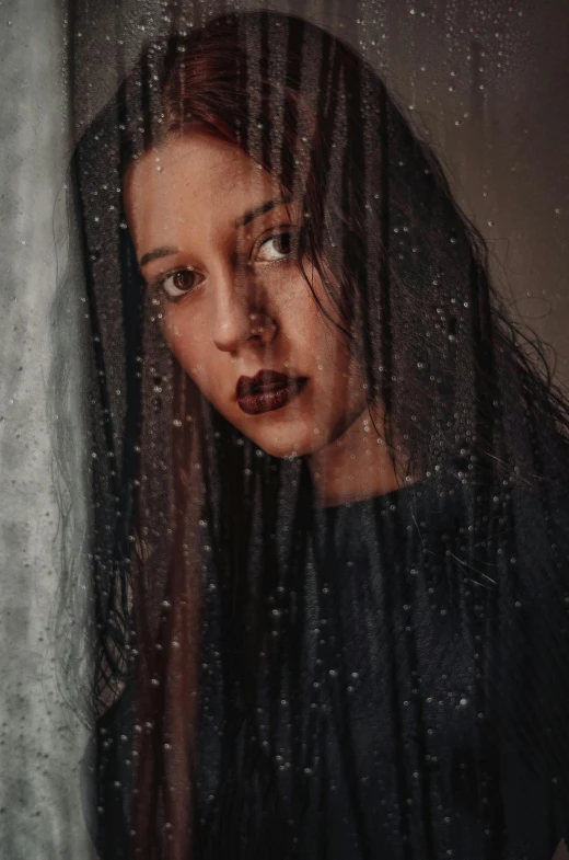 a woman standing next to a window with drops of water