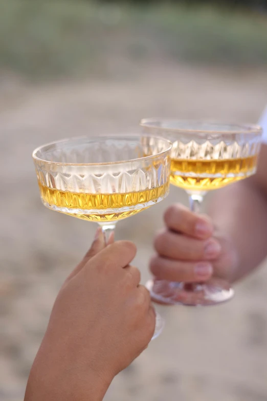 two hands holding up wine glasses filled with liquor